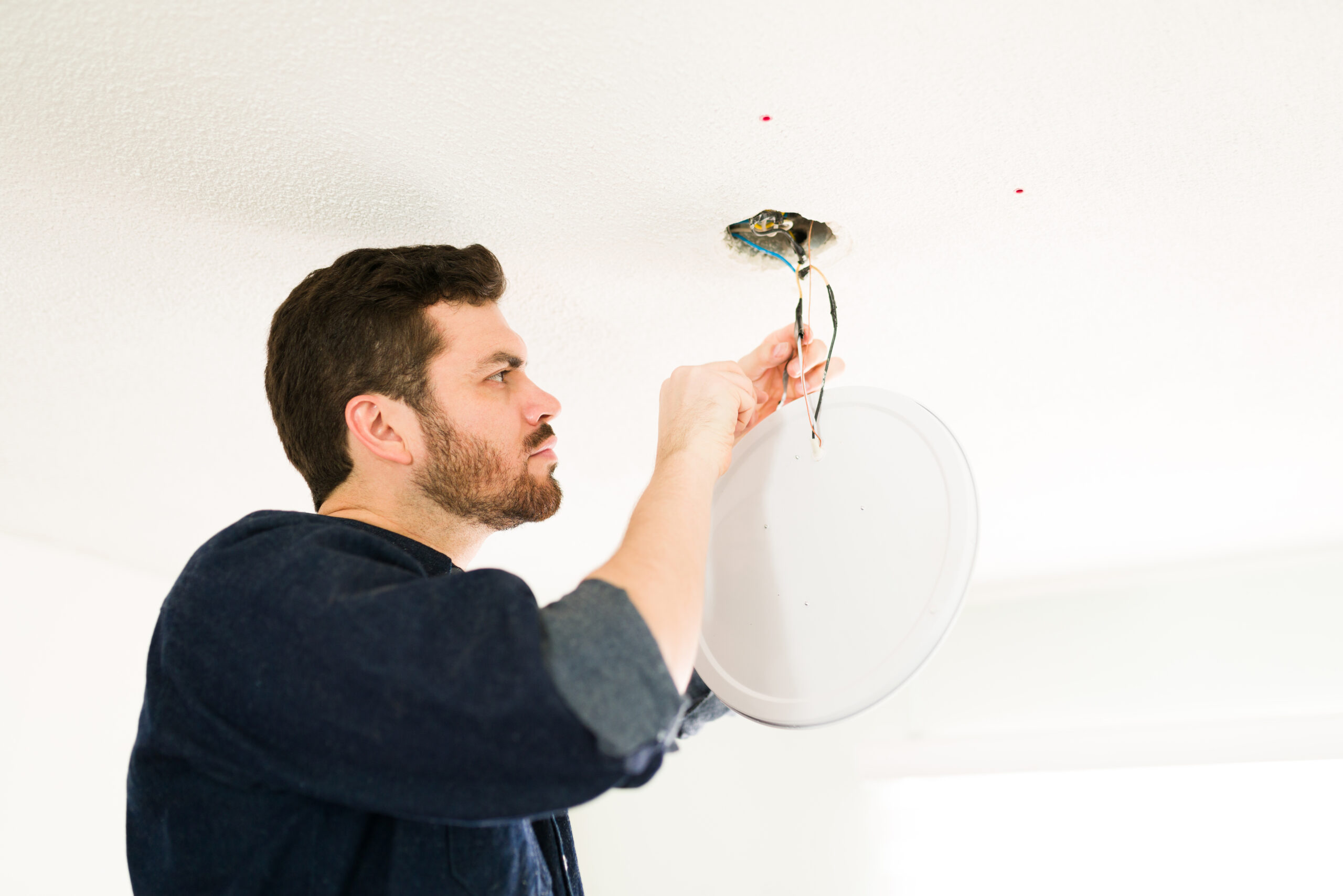 Professional hispanic electrician fixing the electrical system in the ceiling and cutting some cables at home